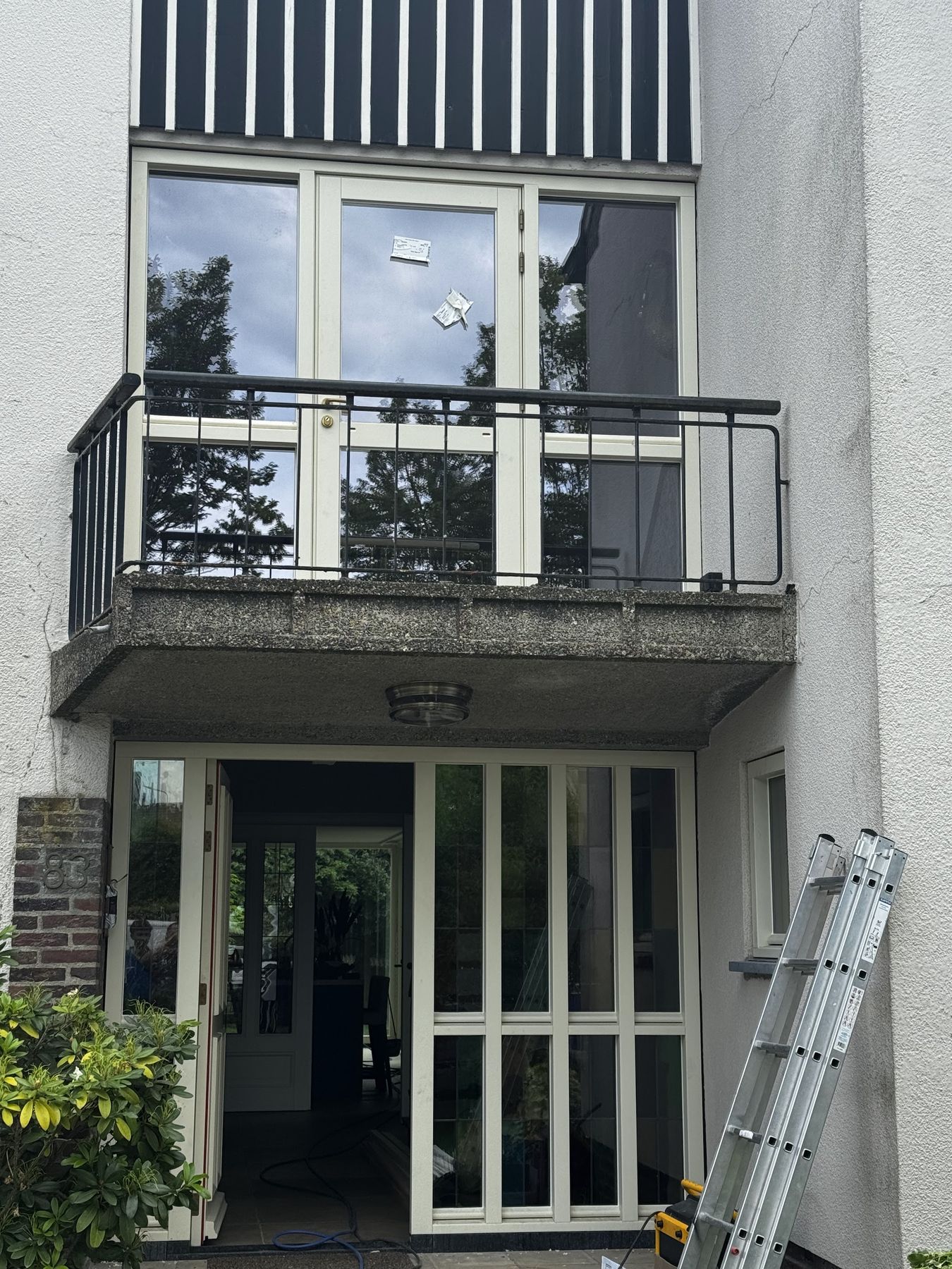 Gevel met nieuw beglaasde balkondeuren boven en een glazen entreepartij beneden, ladder tegen de gevel
