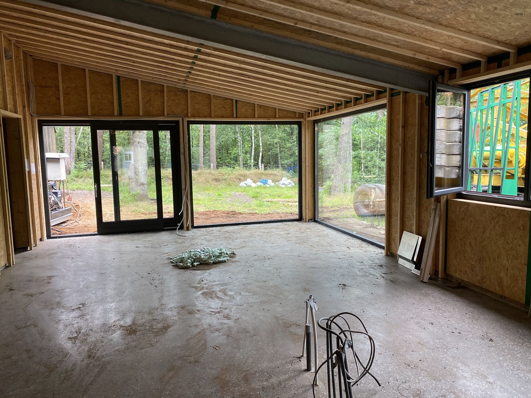 Houtskeletbouw in aanbouw met grote glazen puien en schuifdeuren met uitzicht op bos