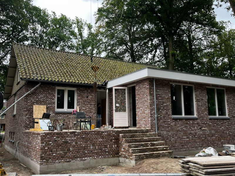 Achterzijde van dezelfde woning met nieuwe ramen en een glazen deur naar het terras